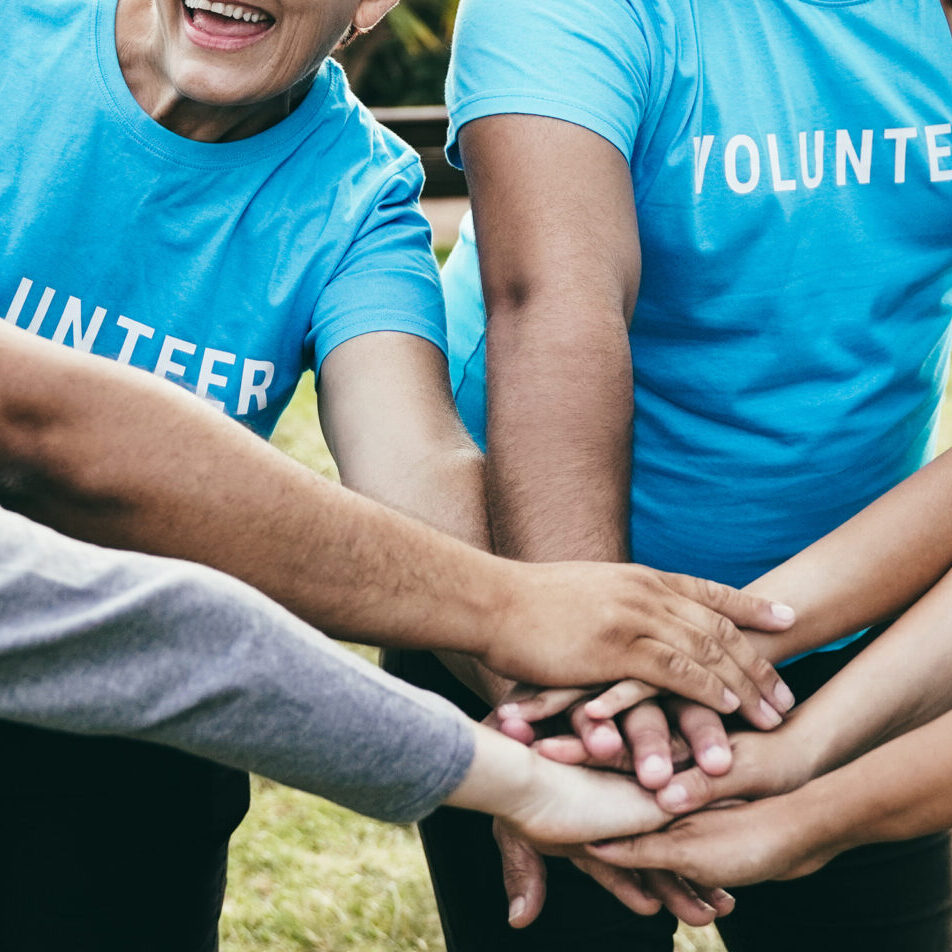 Happy group of volunteer people stacking hands celebrating together outdoor - Teamwork and charity support concept - Focus on back faces